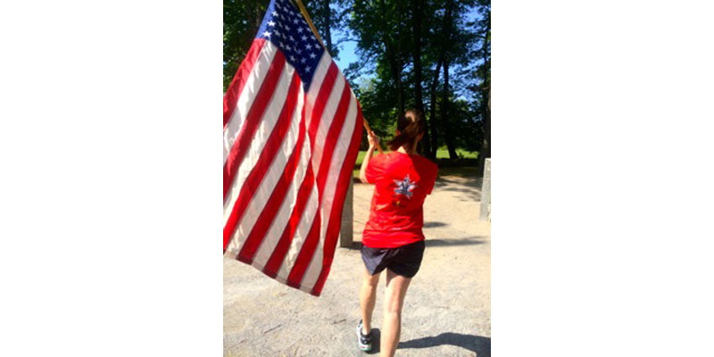 A woman walking down the street holding an american flag.