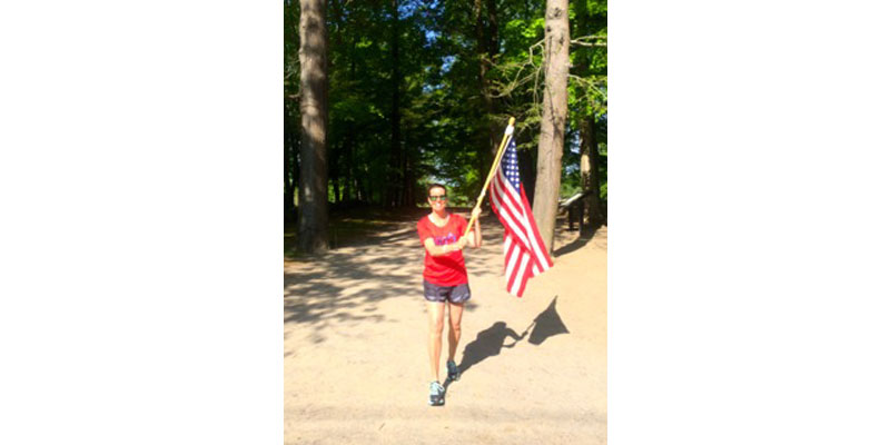 A woman holding an american flag in front of some trees