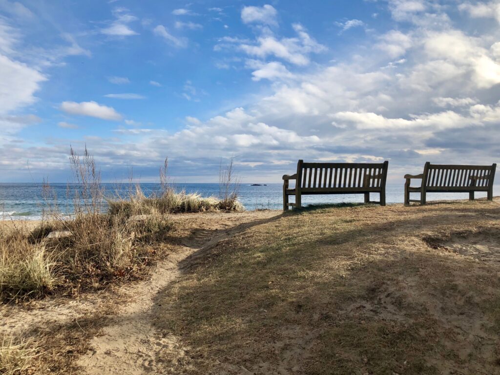 Two benches on a beach near the ocean.